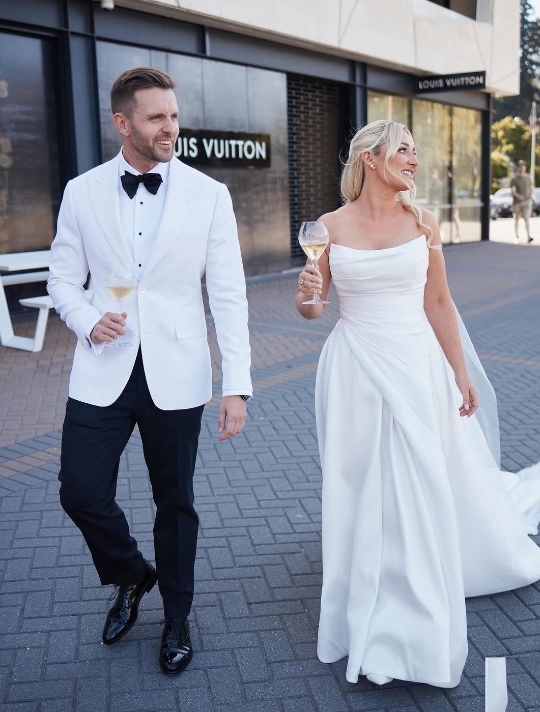 Bride and groom walking through town with their glasses in hand